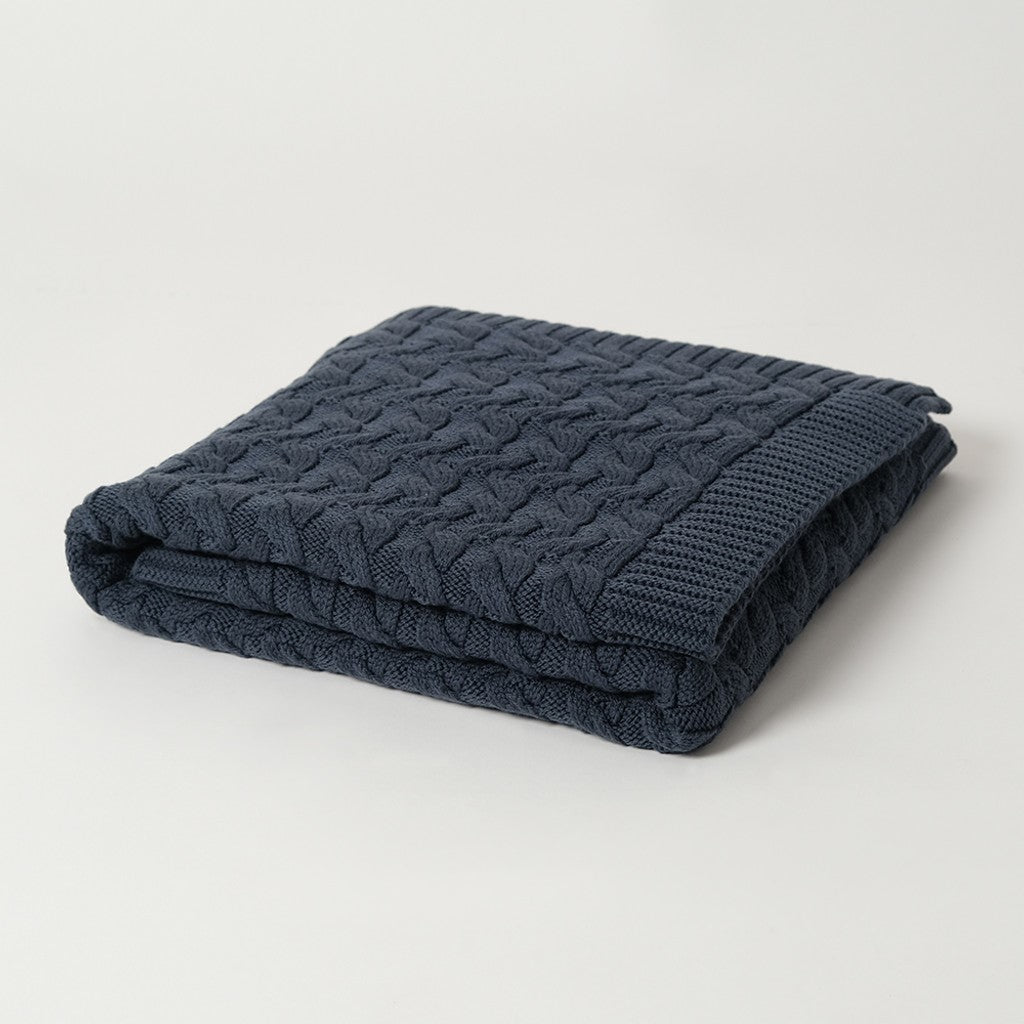 A folded navy blue merino wool blanket with a cable knit pattern,