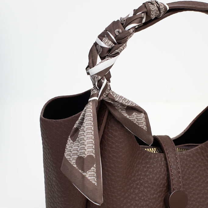 A close-up of a dark brown pebbled leather handbag with a matching brown and beige patterned scarf tied to its handle