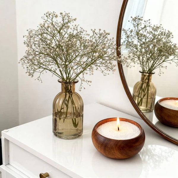 Vase with baby's breath flowers and wooden candle holder on a white surface.