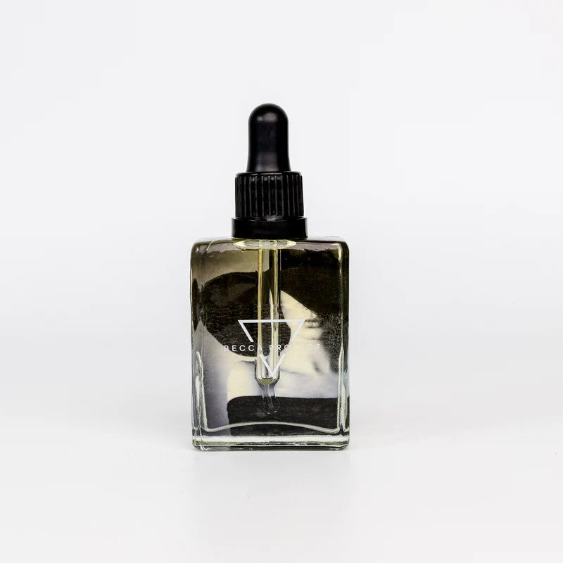 A clear glass bottle with a dropper containing body oil. The label reads 'Becca Project'.