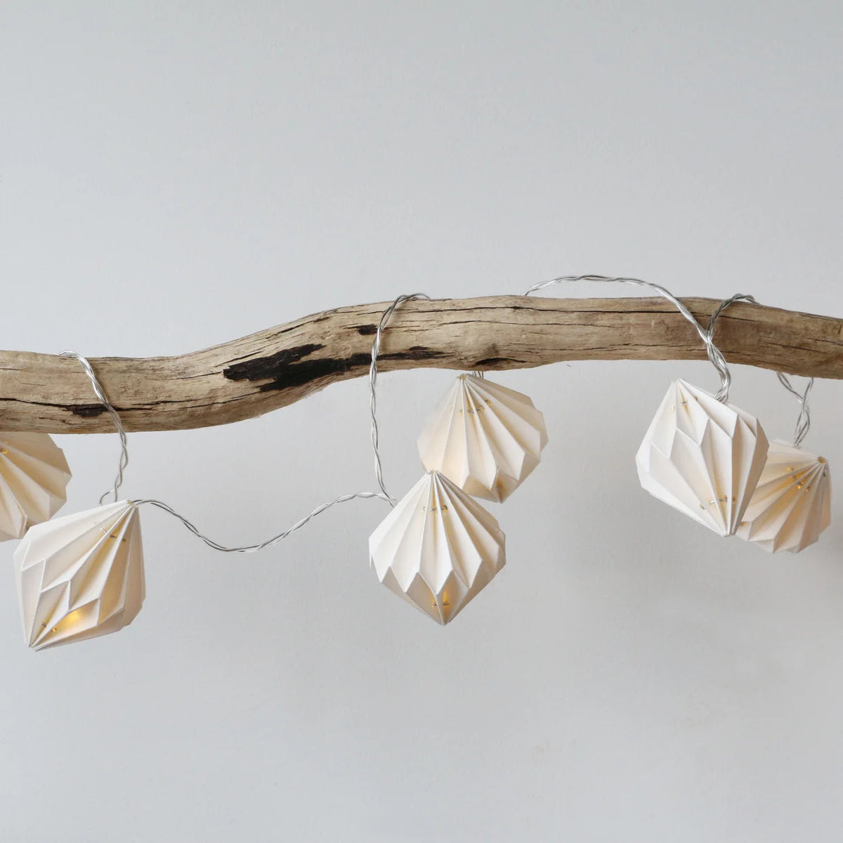 Folding paper lantern string lights in a warm cream color, draped over a rustic natural wood branch