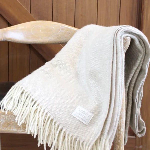 A beige lambswool throw blanket with fringes,