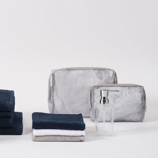 Gray toiletry bag, navy towel, and clear soap dispenser on a white background