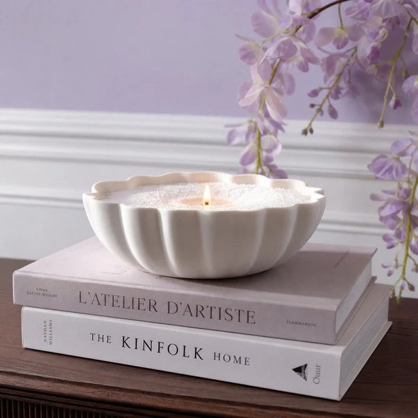 Candle in a decorative bowl on top of books with a purple floral background