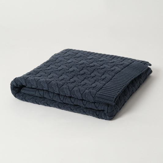 A folded navy blue merino wool blanket with a cable knit pattern,