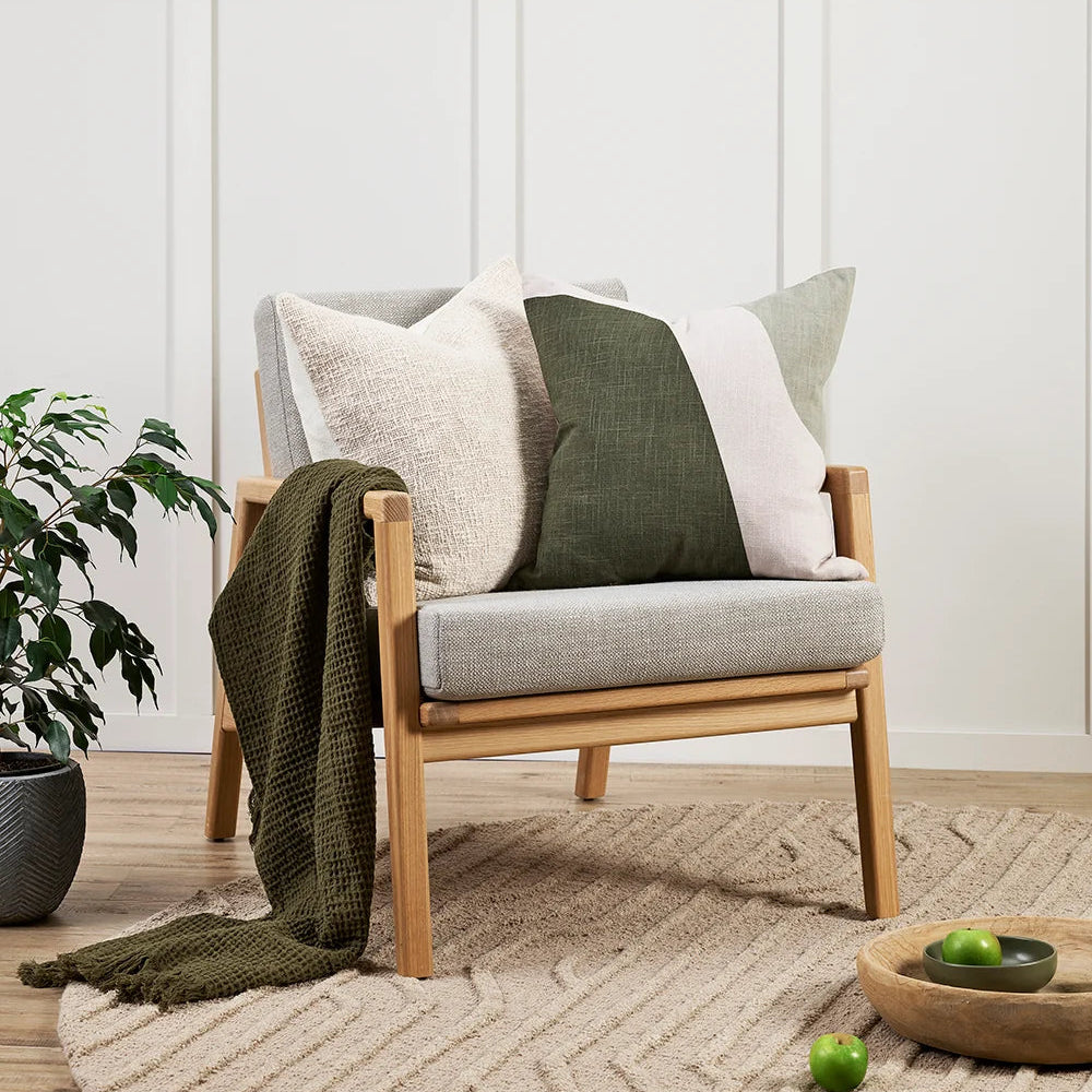Chair with cushions and a blanket in a room with a plant and decor items.