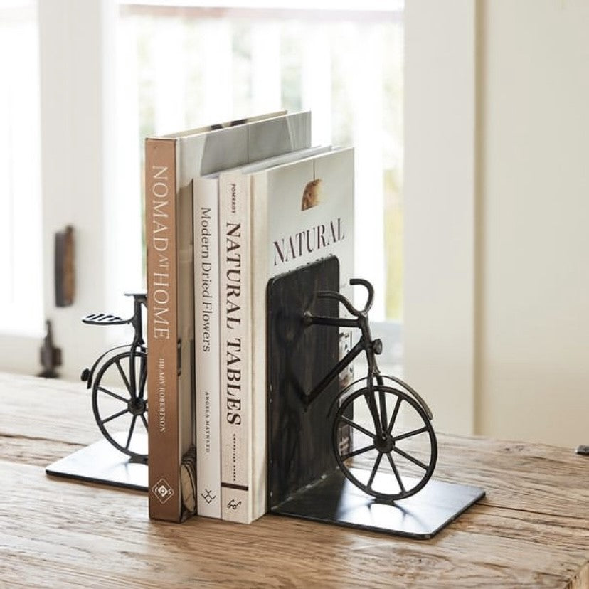 A pair of black bicycle-shaped iron bookends placed on a wooden surface, holding up two books.