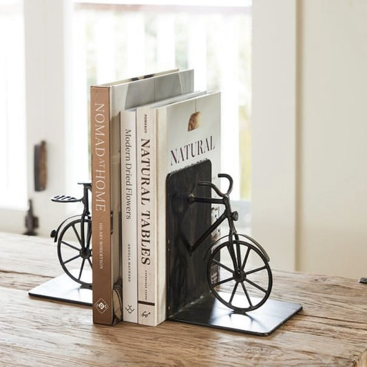 A pair of black bicycle-shaped iron bookends placed on a wooden surface, holding up two books.