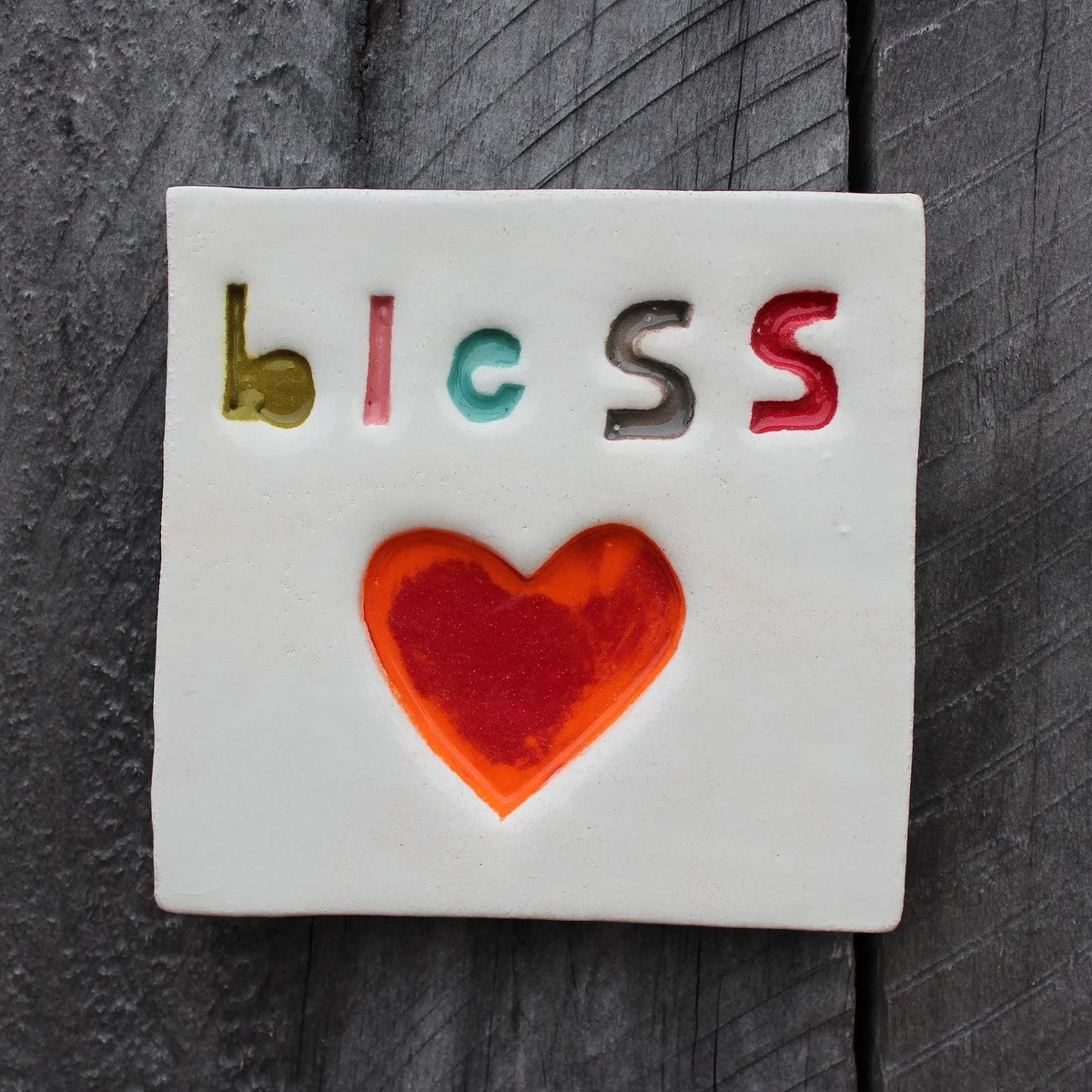 A handcrafted ceramic wall tile with the word 'BLESS' written on it, 