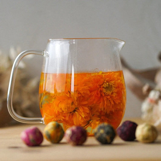 A clear glass teapot with a handle, filled with water and blooming tea balls