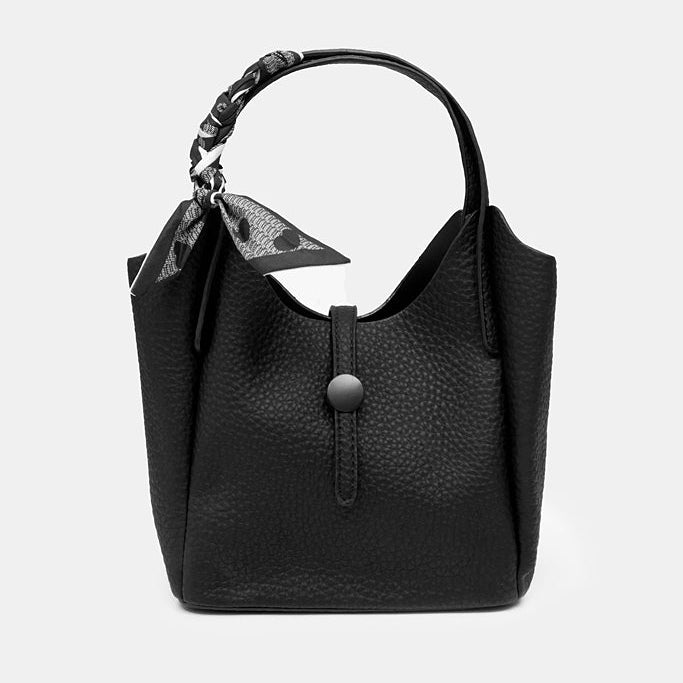 A black pebbled leather top-handle handbag with a decorative black and white patterned scarf tied to the handle, 