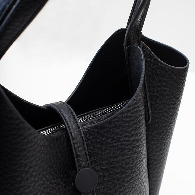 Close-up of a black pebbled leather handbag with a top zipper and a black snap-button strap closure,