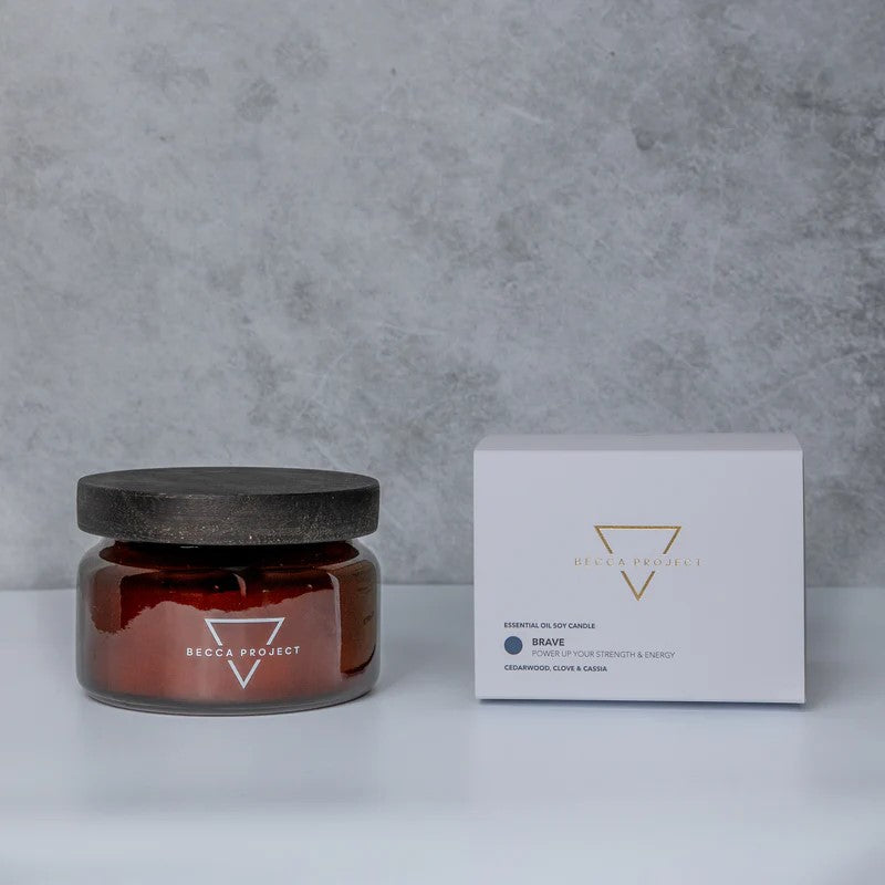 A medium-sized red candle with a black lid, labeled 'Brave Candle' by Becca Project