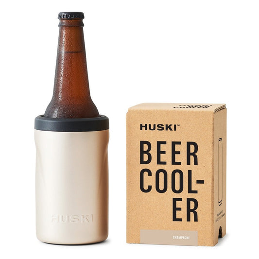 A beige Huski Beer Cooler 2.0 Champagne placed next to its packaging box with the text 'BEER COOLER' on it.