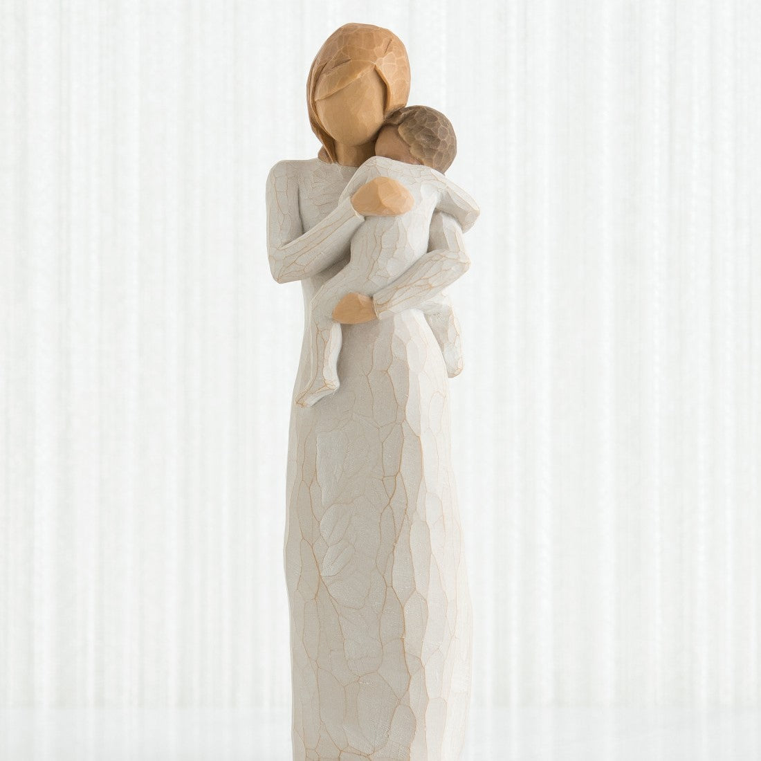 A hand-painted resin figurine of a standing figure in a cream dress holding a toddler in a cream onesie.