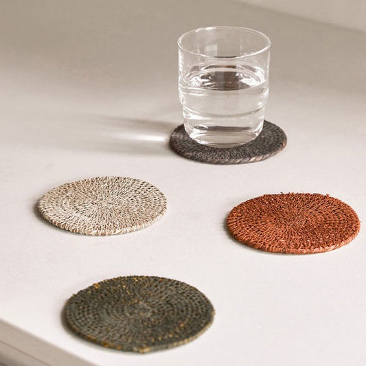 Set of four woven coasters on a white surface with a glass of water.