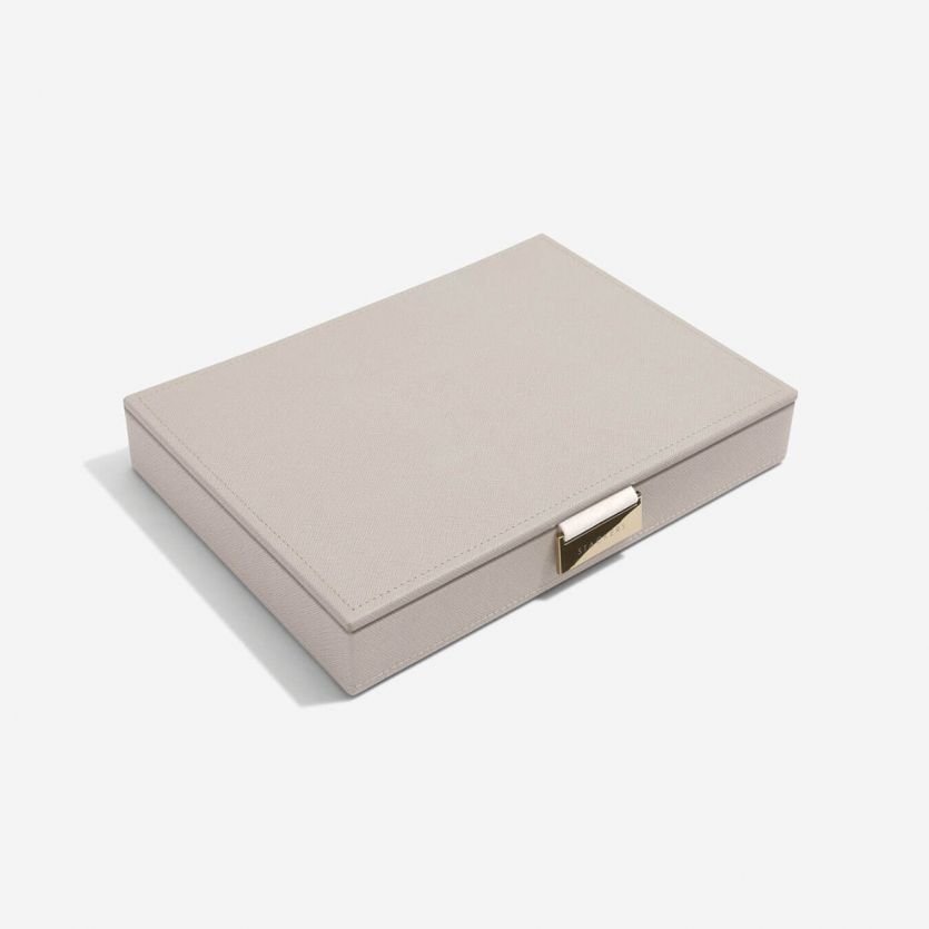 A taupe colored jewellery box lid with a grey velvet interior, featuring a vegan leather exterior and a metal clasp closure.
