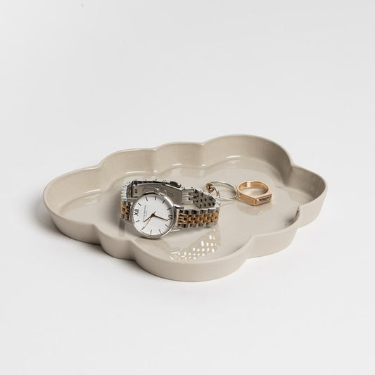 A beige stoneware jewellery tray with a cloud-like shape, displaying a watch and rings on a white background.