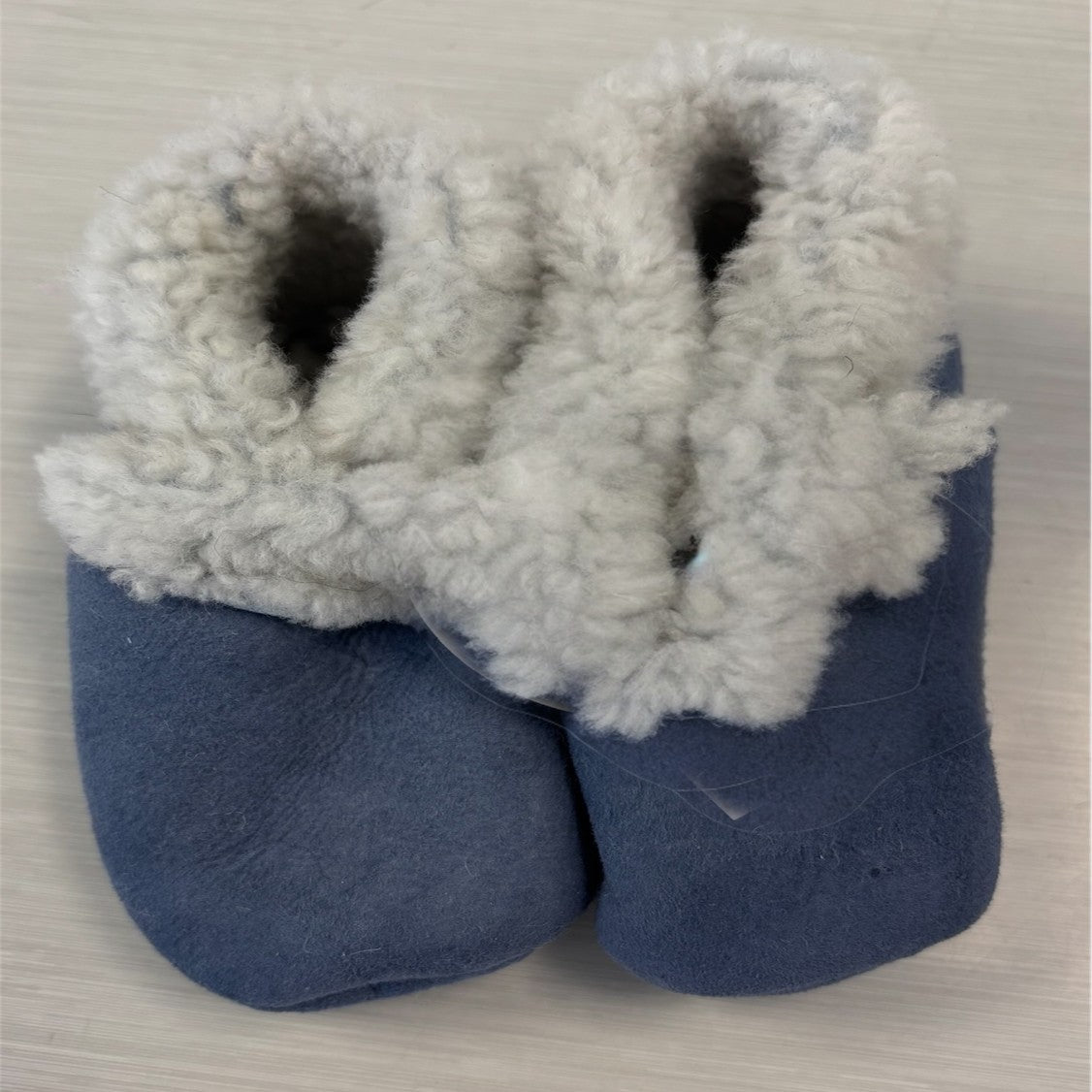 A pair of blue lambskin booties with elastic closure, designed for babies.