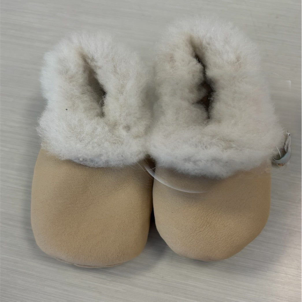 A pair of cream-colored lambskin booties with elastic closures, designed for babies.