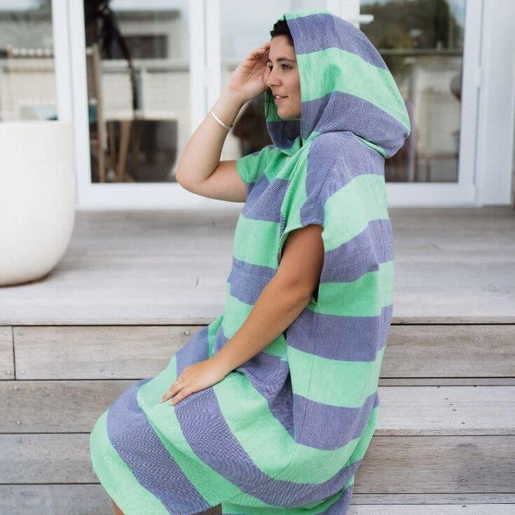 Person wearing a green and blue striped poncho sitting on wooden steps.