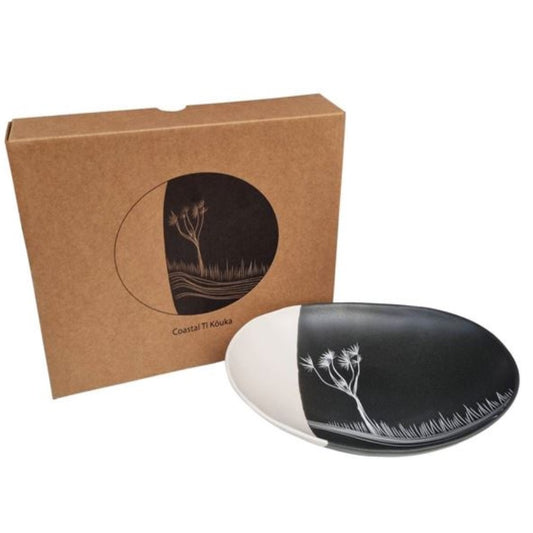 A 24cm bowl with white interior on a black exterior, featuring a coastal ti Kouka design, presented next to its packaging box.