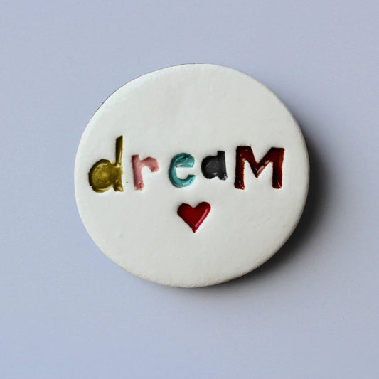 A circular ceramic wall disc with the word 'DREAM' written on it, bordered by a black edge, 