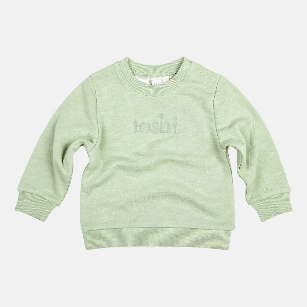 A green organic cotton sweater for babies with the Toshi logo embroidered on it.