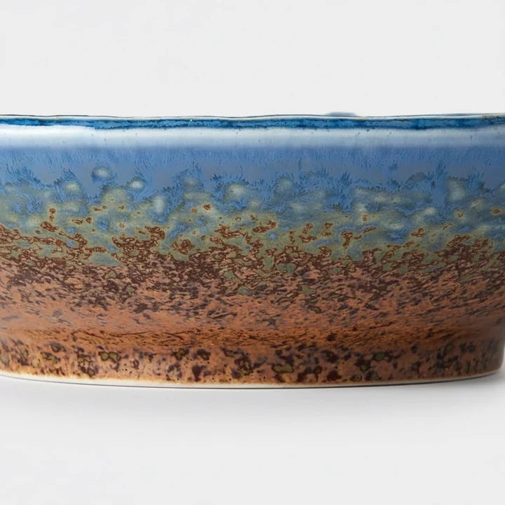 A close-up of a ceramic bowl or planter with a textured glaze transitioning from blue at the top to earthy brown and black speckling at the bottom.
