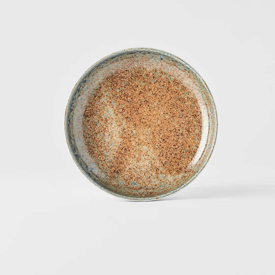 A round ceramic plate with a speckled brown and beige glaze and a blue-green rim, photographed from directly above on a light gray background.