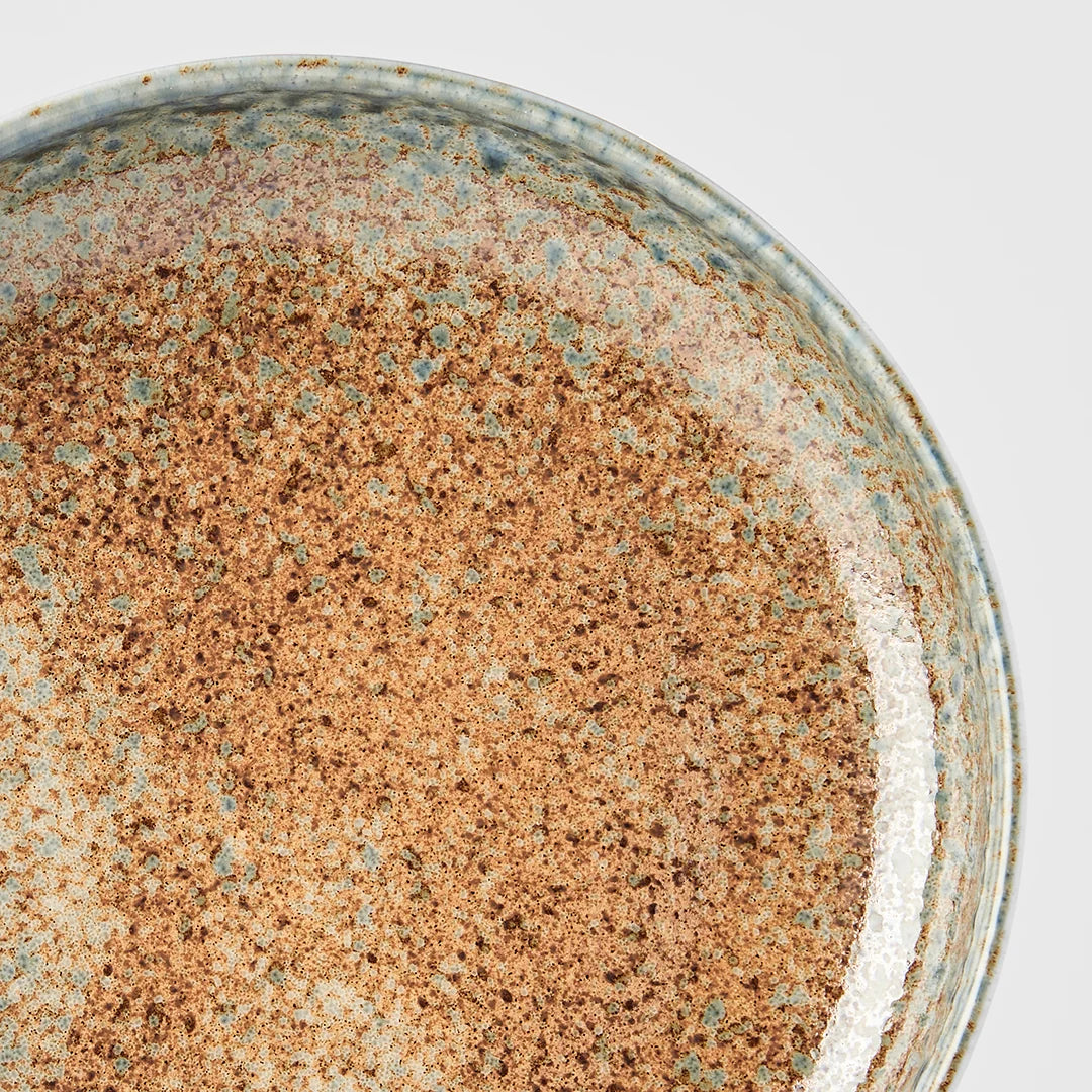 Close-up of a ceramic bowl or dish interior with a speckled earthy glaze in warm brown, tan, and muted blue-green tones.