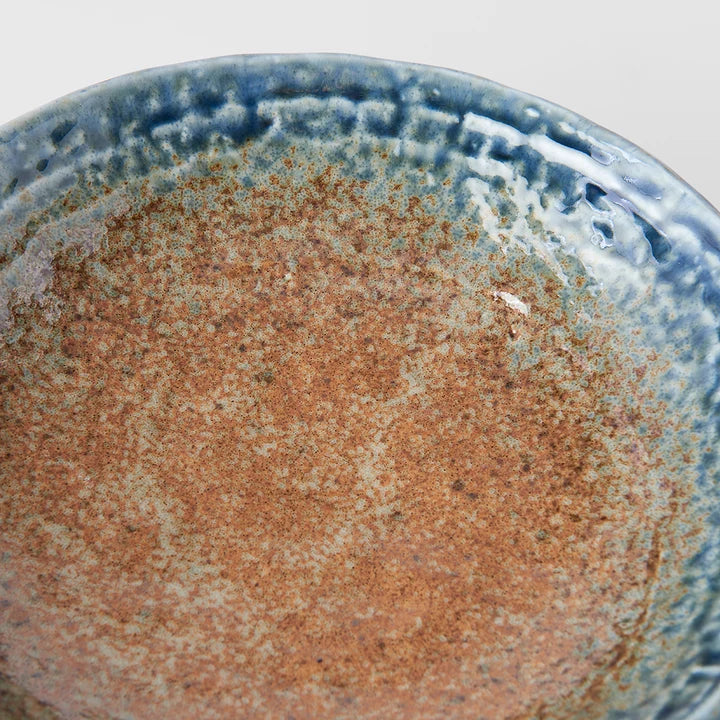 Close-up of a ceramic bowl or plate with a speckled earthy brown center and a blue glazed rim