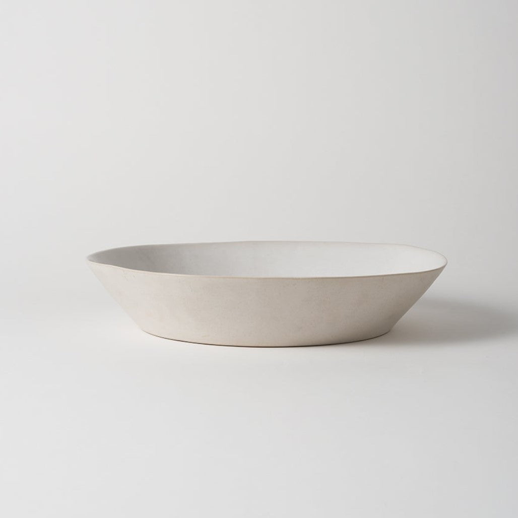 A white, handmade stoneware serving bowl with an organic shape,