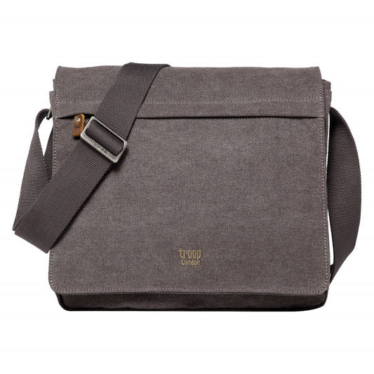 A Troop London front flap messenger bag in charcoal color made from canvas with leather trimmings, featuring an adjustable shoulder strap, a main compartment with a zip closure, and a front flap with a zip pocket and an open-top organizer compartment.