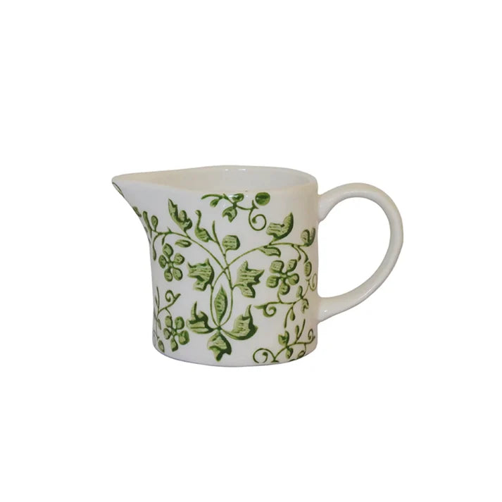 A white ceramic creamer pitcher decorated with a green ivy and leaf pattern, 