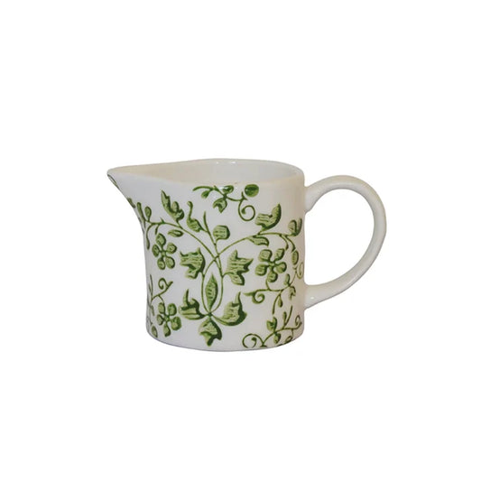 A white ceramic creamer pitcher decorated with a green ivy and leaf pattern, 