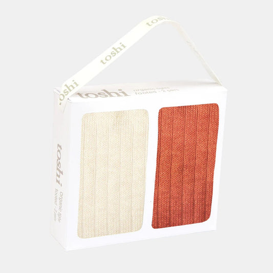 A pair of Toshi footed tights in autumn colors, presented in a white gift box with two color panels: one beige and one red.