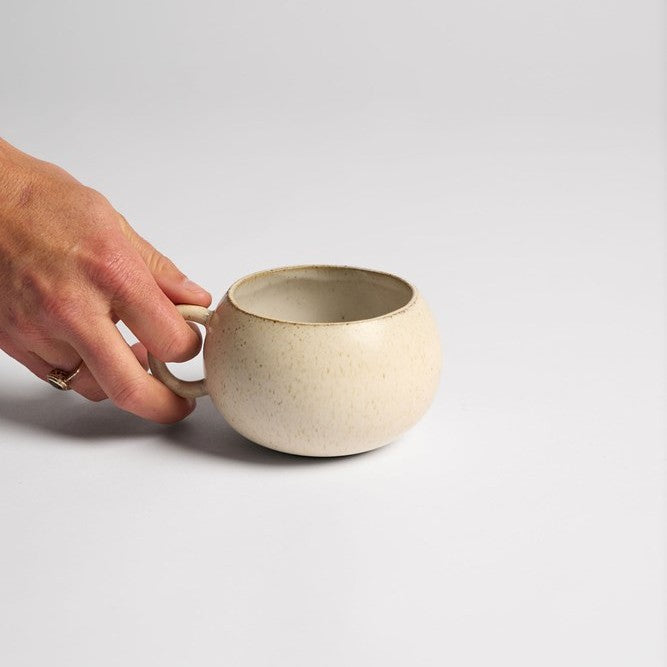 Hand holding a beige ceramic mug on a light gray background