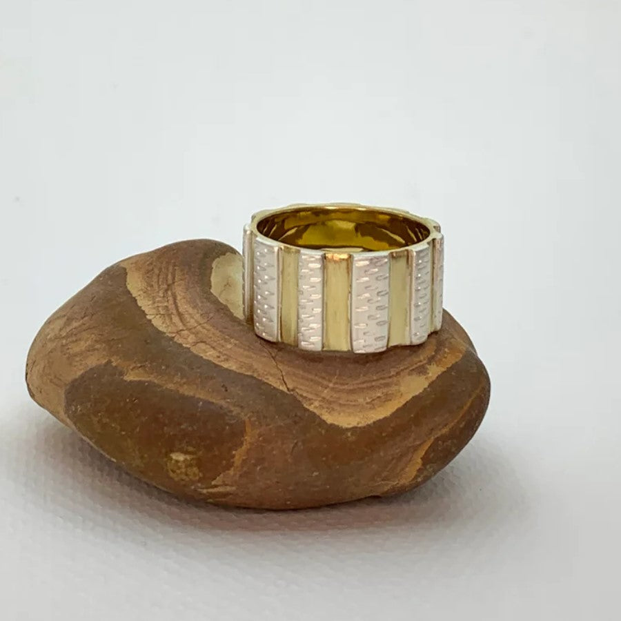A sterling silver ring with a wide band that features vertical stripes of yellow brass and hand-decorated fine etched lines
