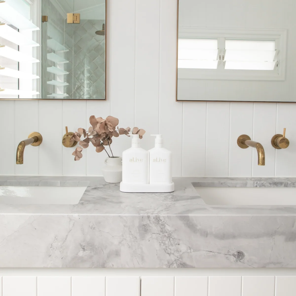 Bathroom vanity with marble countertop, gold fixtures, and a white bottle labeled 'Sculpted'.