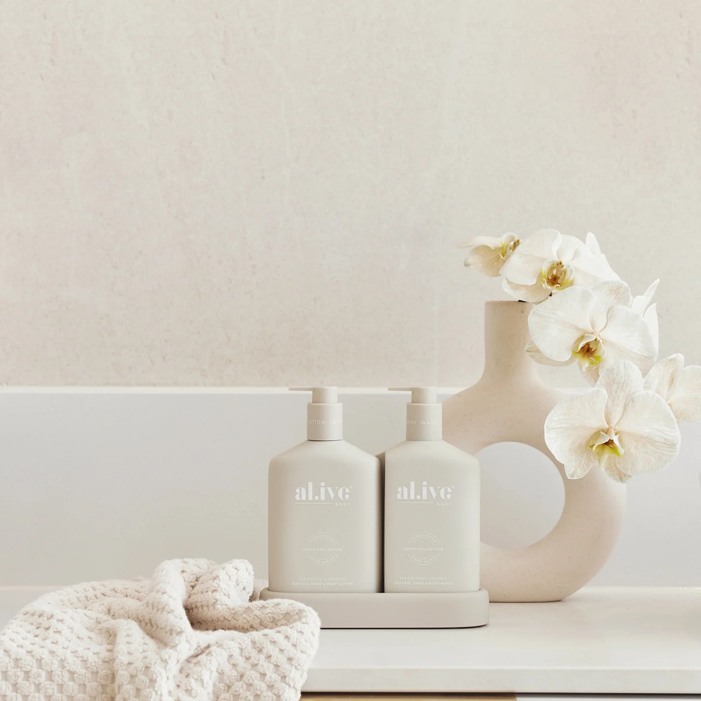Two white bottles labeled 'alive' on a shelf with a vase and flowers against a light background
