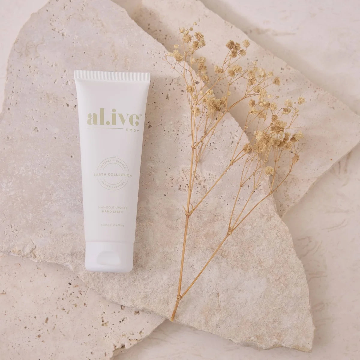 Tube of 'al.ive' cream on a textured stone surface with a dried plant.