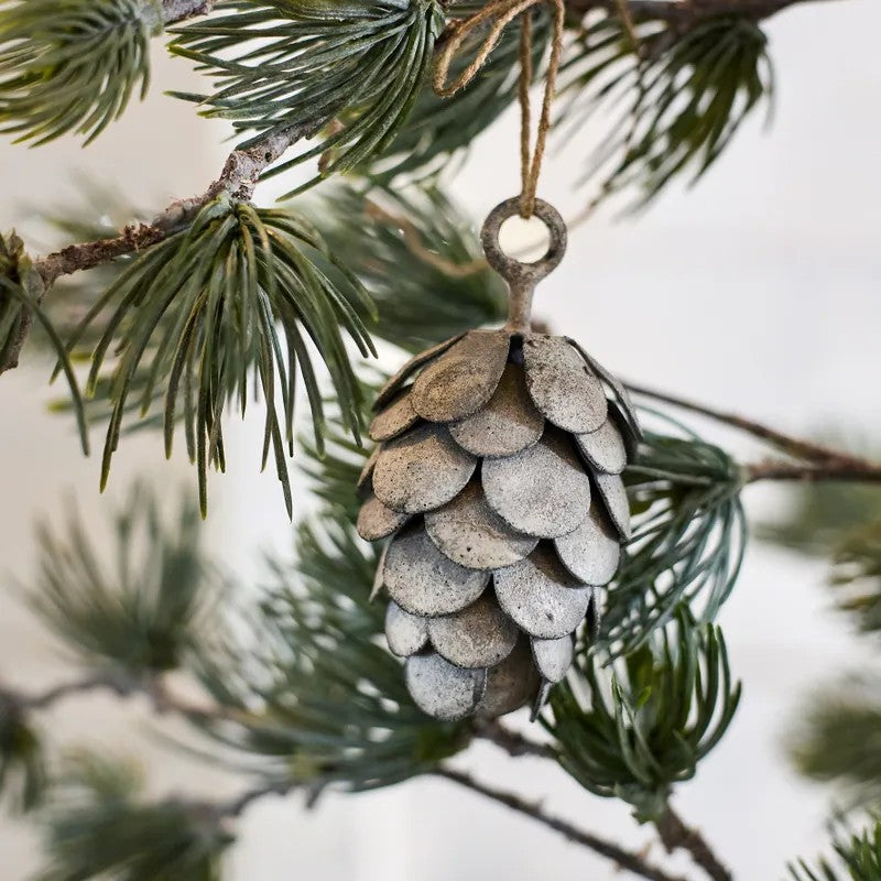 Decorative pine cone ornament hanging on a branch with snow in the background
