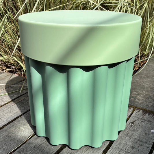 Green ribbed storage container/stool on a wooden surface with grass in the background