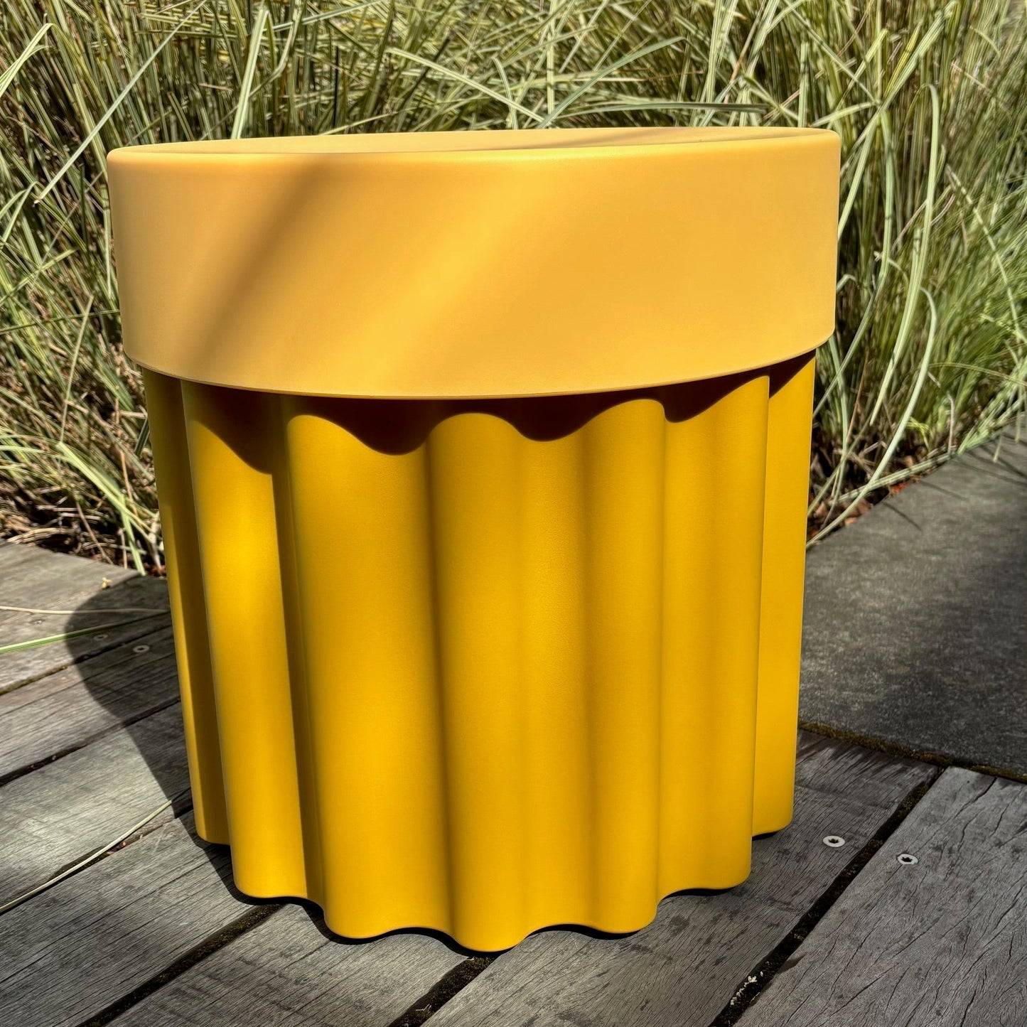 Yellow ribbed container on a wooden deck with grass and blue sky in the background