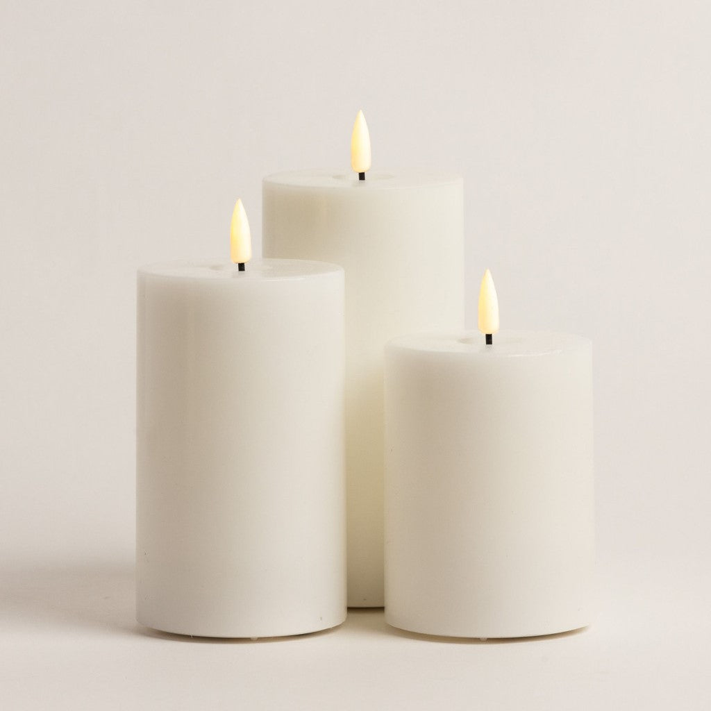 Three ivory pillar candles on a white background, each with a lit wick and yellow tip.