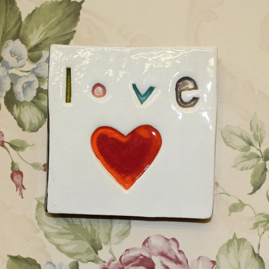 A handmade square ceramic tile with the word 'LOVE' written on it,