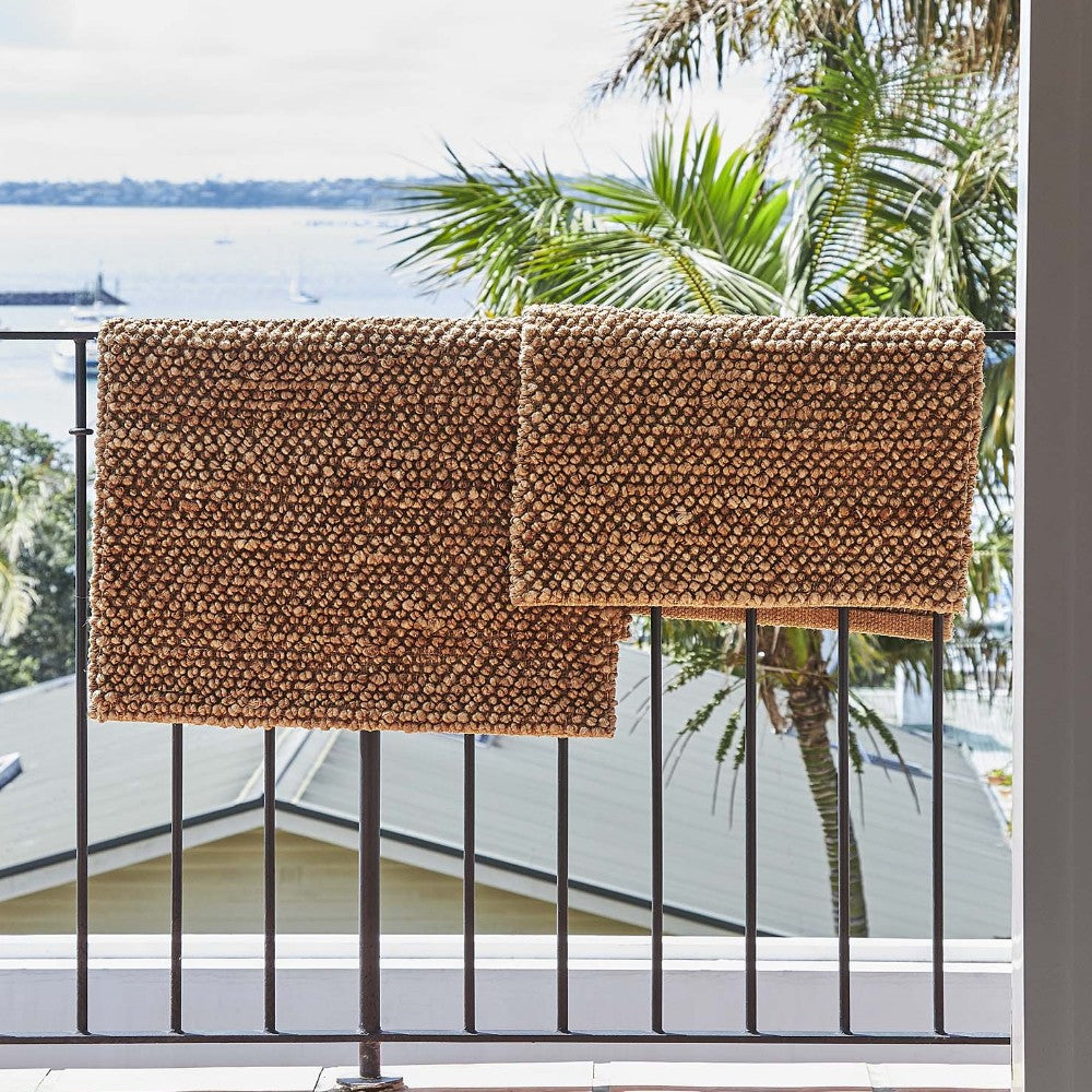 Two woven planters on a balcony with a view of palm trees and water.