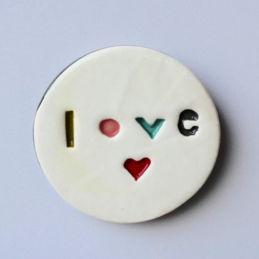 A round ceramic plaque with the word 'LOVE' stamped in the center, with a contemporary palette and a black edge.
