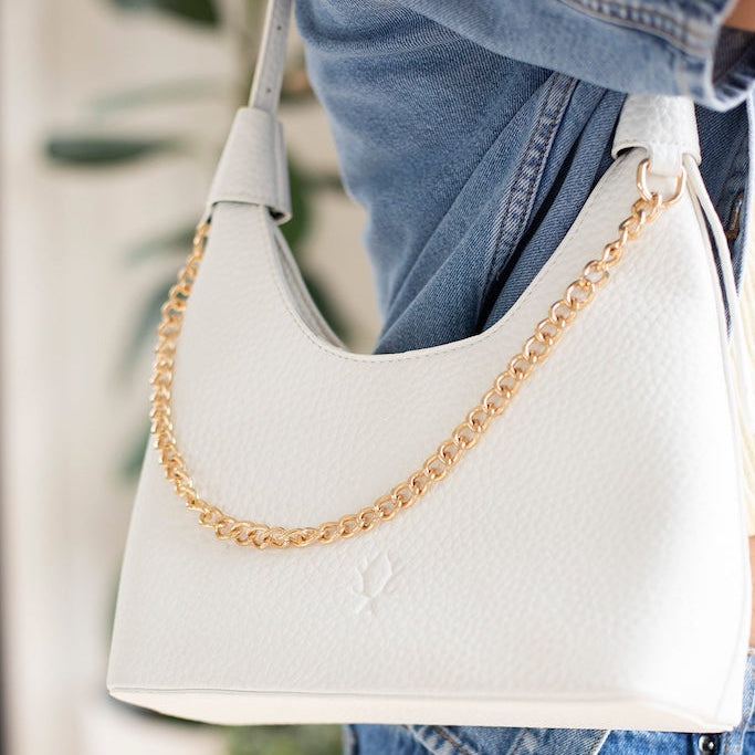 A white pebbled leather shoulder bag with a gold chain strap, worn by a person in a blue denim jacket and jeans.